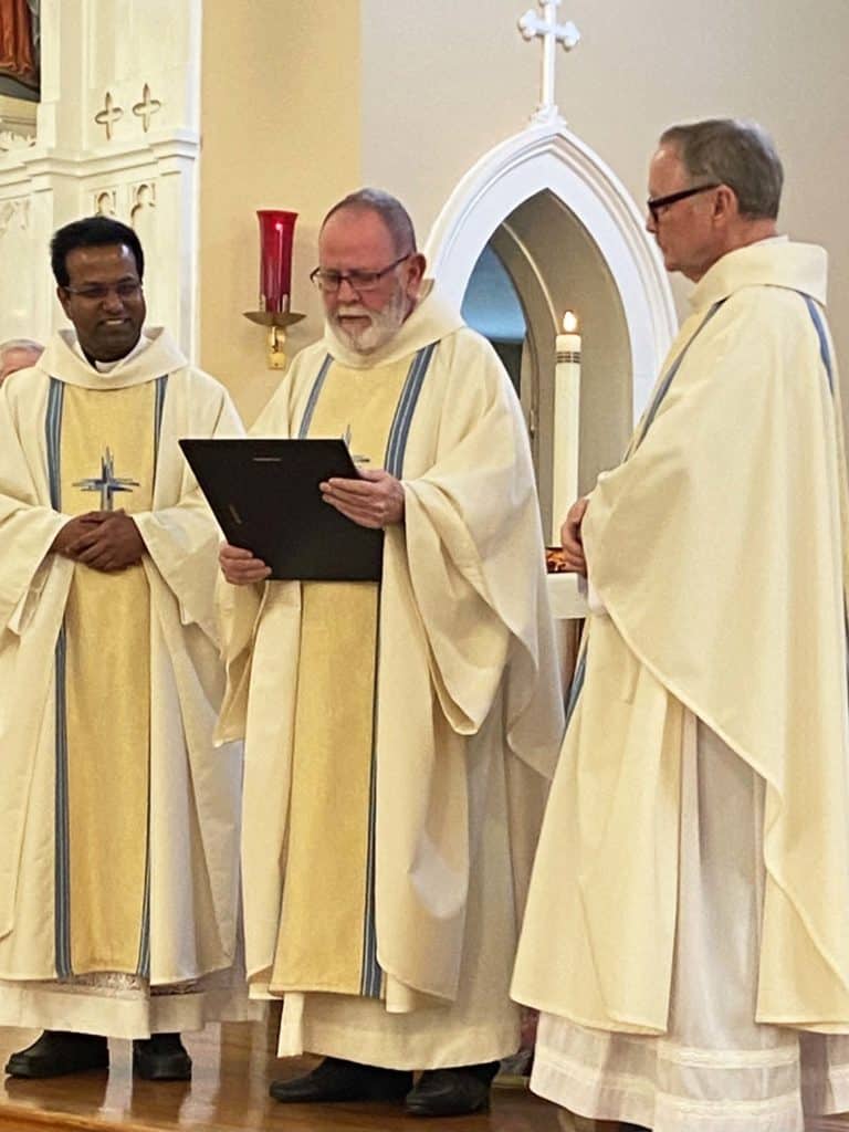 Father George Illikkal, pastor of St. Theresa, left; Father Ron Knott, center, who spearheaded the Family Life Center effort; and Father Bob Ray, nephew of Ursuline Sister Elizabeth Ann Ray who did the research for the center, look at a plaque of appreciation for all their work.