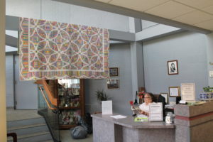 A quilt is on display in the Retreat Center lobby during the Runaway Quilters retreat. Seated at the front reception desk is Sister Lois Lindle.