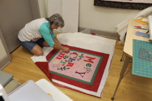 Marilyn Adkins of Sacramento, Ky., sits on the floor as she puts a binding on her wall hanging.