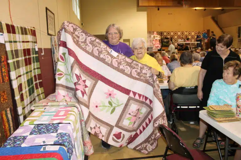 Ann Jacobs of Moscow Mills, Mo., niece of the late Sister Amelia Stenger, holds the “Neapolitan” quilt that she won. Sister Cecelia Joseph Olinger helps her hold it. Ann Jacobs of Moscow Mills, Mo., niece of the late Sister Amelia Stenger, holds the “Neapolitan” quilt that she won. Sister Cecelia Joseph Olinger helps her hold it.