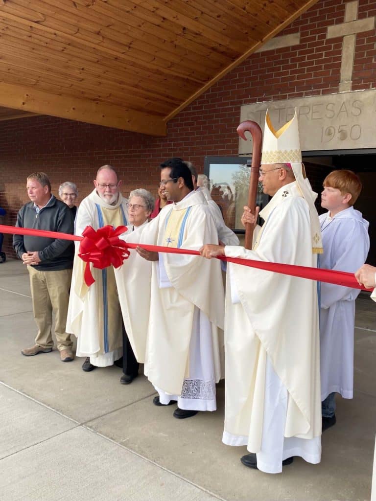 Archbishop Shelton Fabre of the Archdiocese of Louisville, right, helps hold the ribbon as Father George Illikkal, Father Ron Knott and Sister of Charity David Clare Reasbeck prepare to cut the ribbon on the Family Life Center. Sister David Clare served at St. Theresa for many years. In the background left is Ursuline Sister Ann Patrice Cecil.