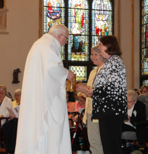 Lea Dorth Clark, center, and Mary Lou Dorth Howard, both A69, deliver the offertory gifts to Father Ray Goetz.