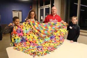 A family holds up a finished children’s blanket.
