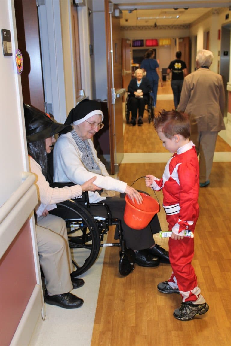 Sister Cecilia Joseph Olinger, left, put on her witch hat and wig to greet the children. She was assisted by Sister Helen Leo Ebelhar, who gives candy to “Power Ranger” Asher.