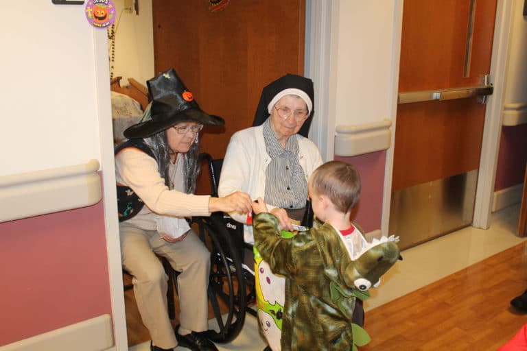 Sister Cecilia Joseph Olinger, left, donned a witch hat and wig for the party. She was assisted by Sister Helen Leo Ebelhar as they gave candy to “Dinosaur” Kaiser.