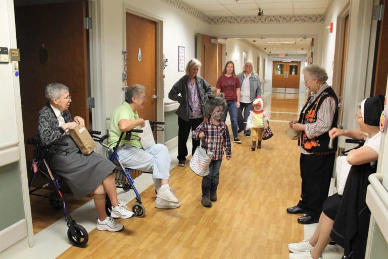 The sisters are happy to see “Wolf” Emmitt and “Chicken” Scarlet as they make their way down the hall to trick or treat. The two sisters seated at left are Sister Amanda Rose Mahoney and Emma Anne Munsterman, while the two at right are Sister Marie Joseph Coomes, standing, and Sister Rose Karen Johnson.