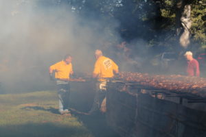 Volunteers brave the smoke to turn over a rack of barbecue chickens on the pit on picnic morning.