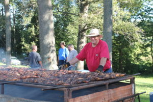 A volunteer smiles as he checks on the barbecue chicken that will feed a crowd that day.