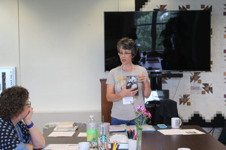 Presenter Heather Berndt explains how to make a SoulCollage® as she holds up an example of a card she made. She encourages people to use their intuition rather than logic when making their cards.