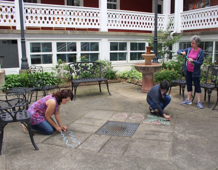 Stacy Green, left, and presenter Heather Berndt of Spokane, Wash., draw with chalk as Karen Stewart of Evansville, Ind., opens a bubble wand in the Retreat Center courtyard. The group took a recess to engage in outdoor play on Saturday.