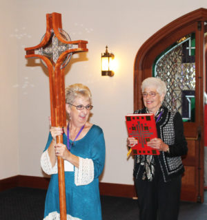 Mary Ann Shewmaker Payne A72, left, prepares to carry in the cross as she shares a laugh with Virginia Ford Green A57, who carried the lectionary.