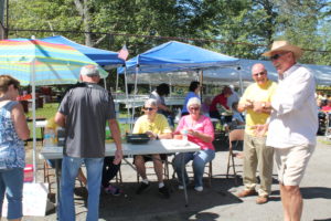 Ursuline Associates John Little and Karen Lasher (seated) and Ed Cecil (standing to their right) help sell dinner tickets during the picnic.