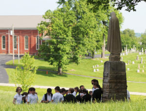 With St. Alphonsus Church in the background, the sixth-graders gather at the feet of the Our Lady of Fatima statue during the scavenger hunt.