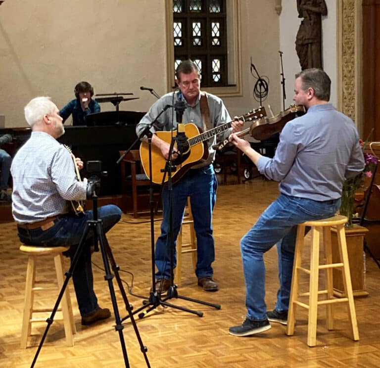 Chris Joslin, left, on mandolin; Chris Armstrong, center, on guitar; and Randy Lanham on fiddle play music as technicians record in the background.