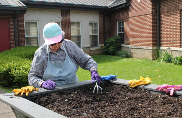 Sister Marie Joseph Coomes uses a garden hand rake to loosen the soil in the flower bed.