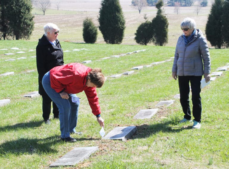 Aloma Dew places a flag on the grave of Sister Francesca Hazel, as Sister Suzanne Sims, left, and Judy Adams discuss her. Sister Francesca founded the Contemporary Woman Program at Brescia College, one of the first programs in the country to focus on helping women value themselves.