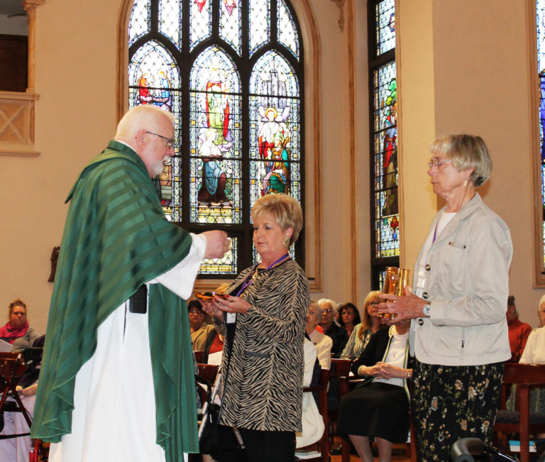 Sandi Bell Boswell A67, center, and Mary Ford Vuncannon A55, present the offertory gifts to Father Ray Goetz.