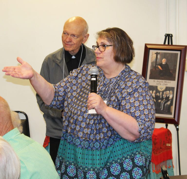 Ursuline Associate Joanne Thompson, of Paola, Kan., shares a topic from her table, as Father Joe Merkt looks on.