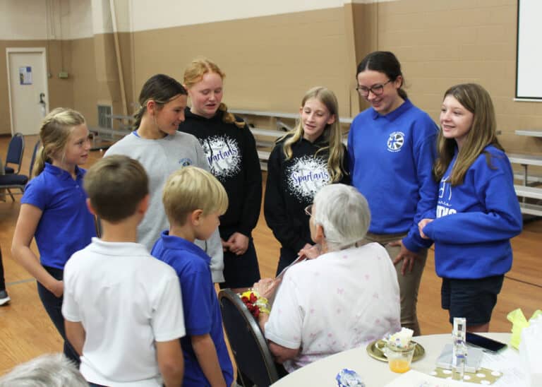 Mary Carrico students gather around Sister Mary Celine to present her with a poster congratulating her.
