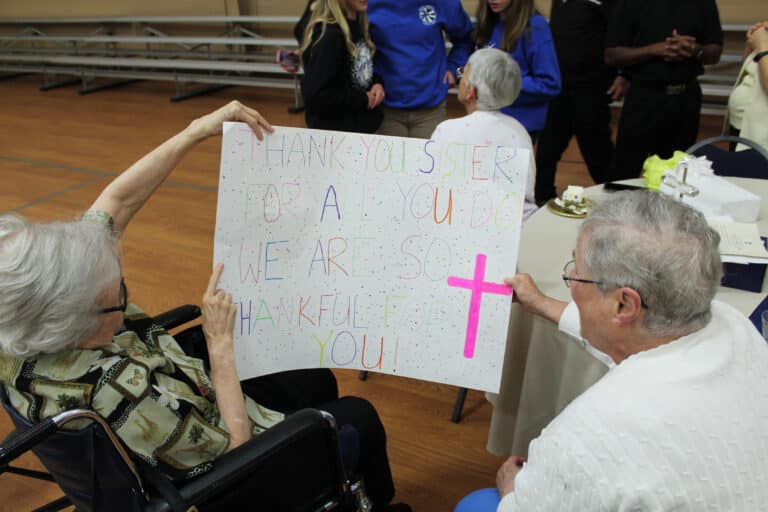 Sister Pat Rhoten, left, and Sister Karla Kaelin hold up the poster given to Sister Mary Celine, which reads “Thank you Sister for all you do. We are so thankful for you!” The students signed the back.
