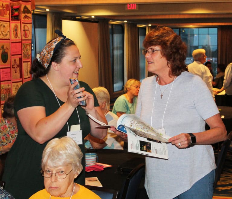 Ursuline Associate Renee Schultz shows Ursuline Associate Doreen Abbott a picture on her phone. The two were both attending their first Ursuline Convocation. Seated is Ursuline Sister Angela Fitzpatrick.