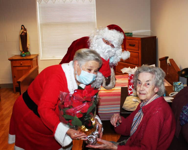 Sister Mary Gerald Payne is excited to receive her poinsettia from Santa and Mrs. Claus.
