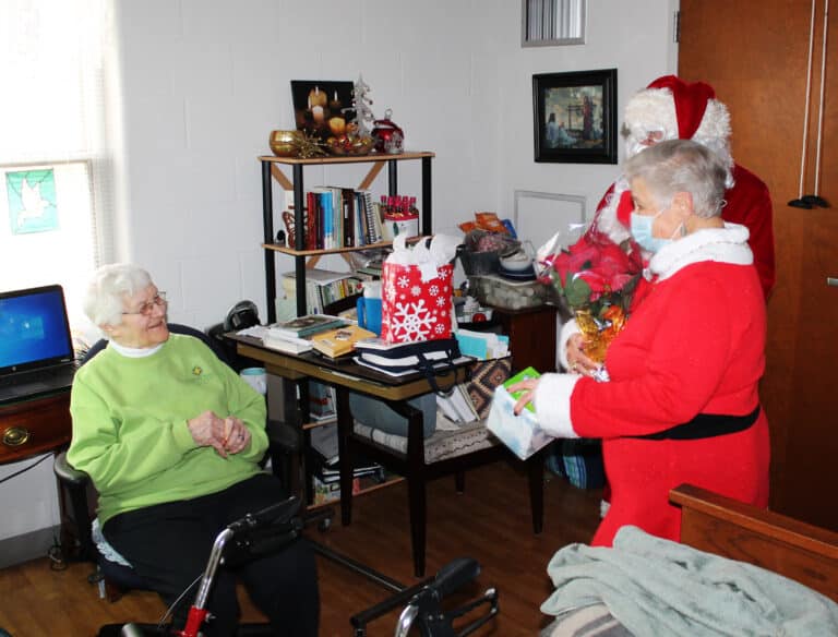 Sister Mary Matthias Ward smiles as Jolly Ol’ Saint Nick and Mrs. Claus bring her presents.