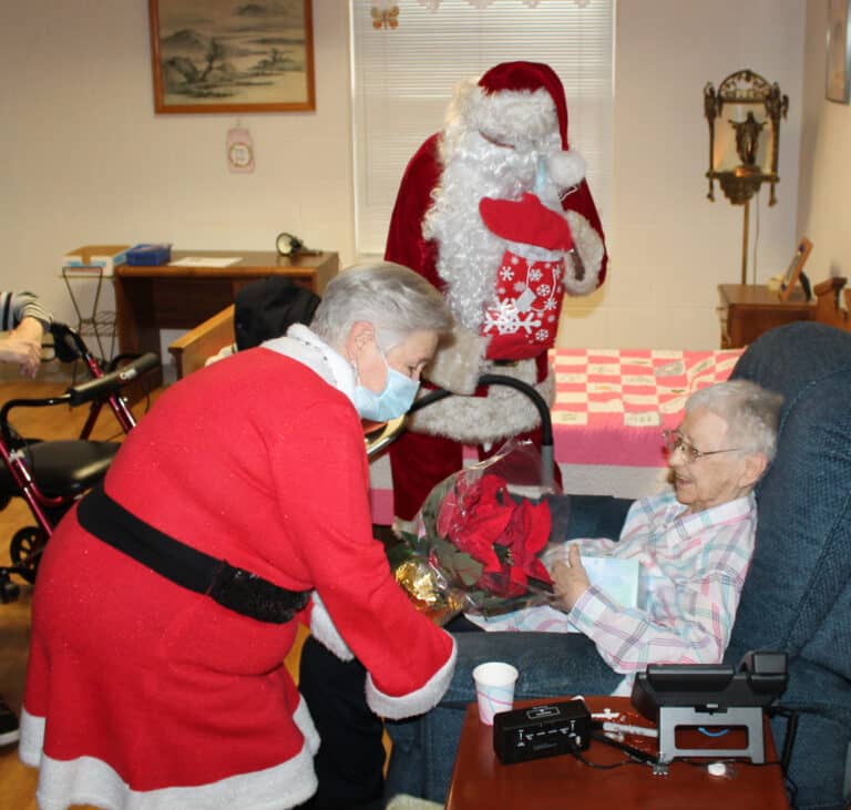 Sister Marie Bosco Wathen, the oldest Sister in the community at 99, smiles as Mrs. Claus brings her a poinsettia.