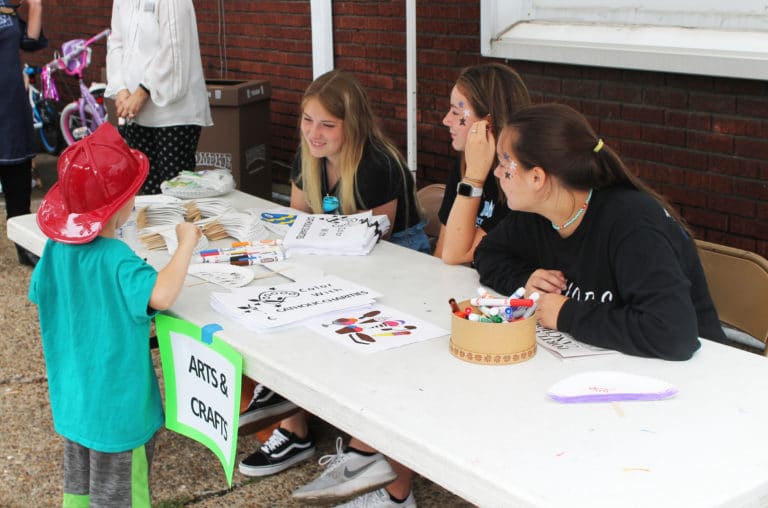 This young firefighter gets some coloring advice from high school students volunteering at the Arts & Crafts booth.