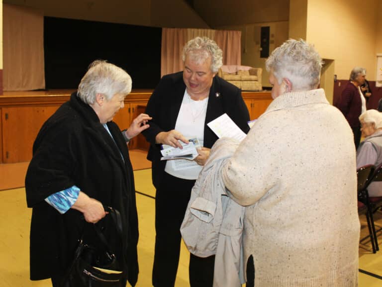 Sister Martha Keller, center, a member of the 150th Celebration Planning Committee, hands programs to Ursuline Associates Donna Favors, left, and Karen Wells.