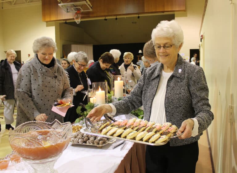 Sister Barbara Jean Head holds a tray of buttermilk cookies as Ursuline Associate Suzanne Reiss, Sister Judith Nell Riney and Associate Bonnie Marks pass through the food line. Sister Amelia Stenger and other Sisters made the cookies and bourbon balls for the event.