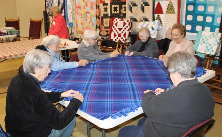 From left, Ursuline Sisters Maureen O’Neill, Elaine Burke, George Mary Hagan, Marie Joseph Coomes, Susan Mary Mudd and Rose Jean Powers work on a blanket together. In the background is Ursuline Associate Carol Hill.