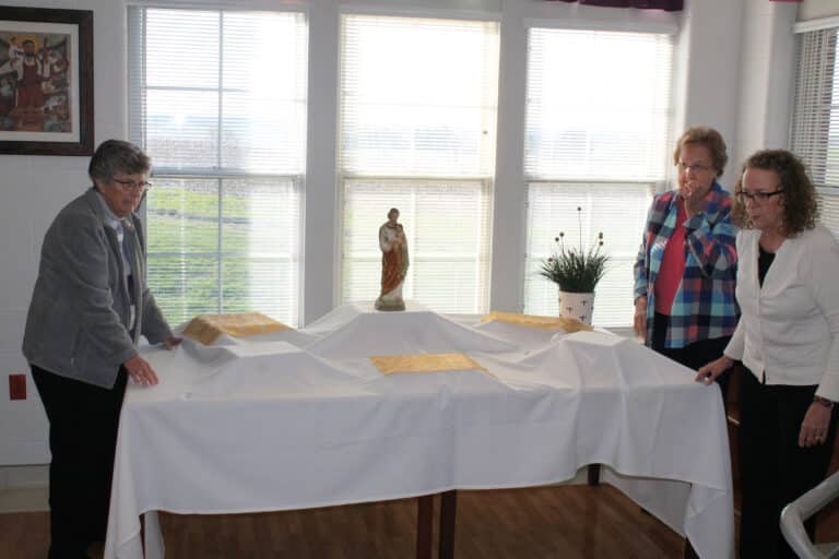 Sister Margaret Ann Aull, left, and Sister Susan Mary Mudd, center, join Ashley Wilkerson, the activities coordinator for the Sisters in the Villa, in setting up Saint Joseph’s Table.