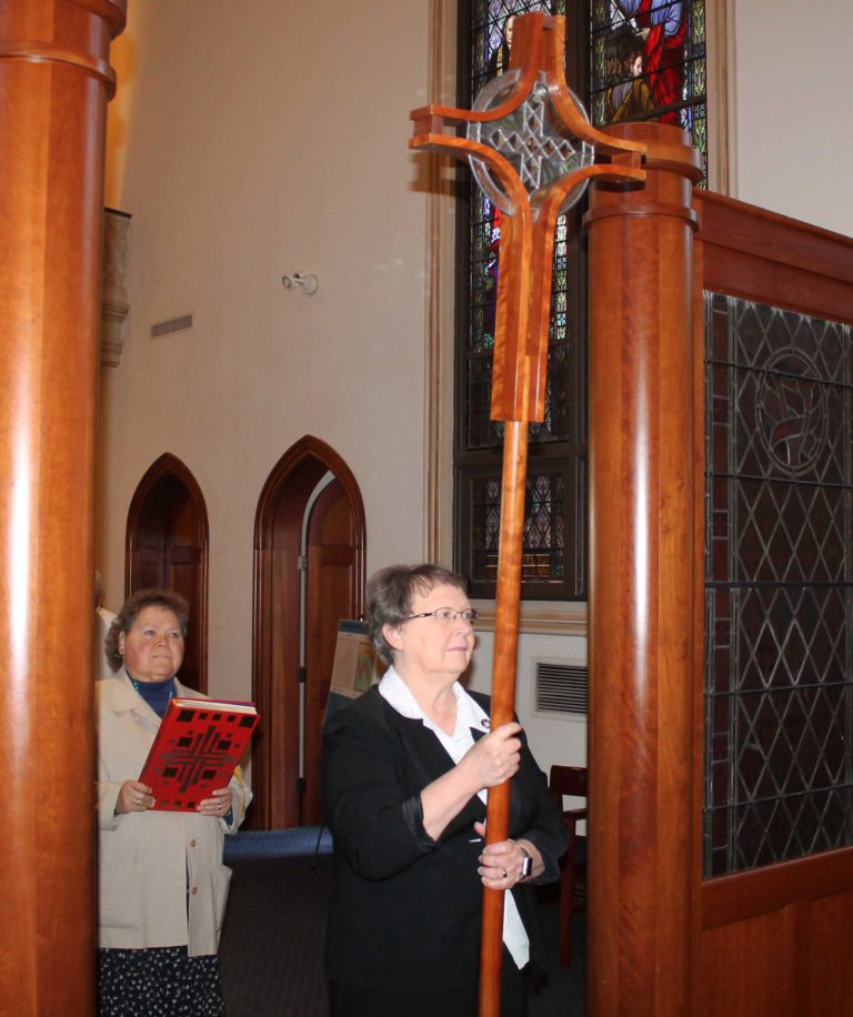 Sister Amelia Stenger carries the processional cross as Sister Alicia Coomes prepares to carry the lectionary to begin Mass.