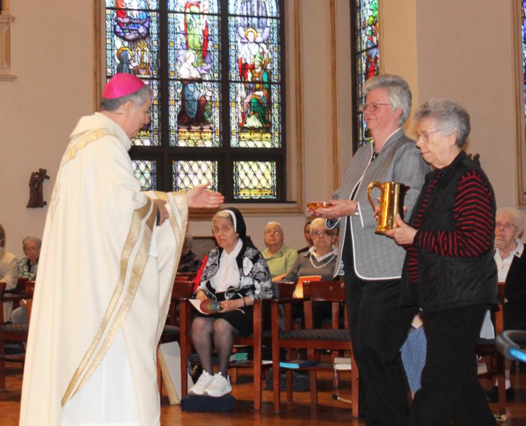 Sister Nancy Murphy, right, and Sister Mary Timothy Bland present the gifts to Bishop William Medley.