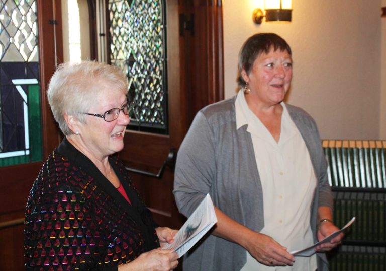Marian Lanham, A73, and Brenda Dant McIntire, A73, share a laugh as Lanham handed out liturgy guides.