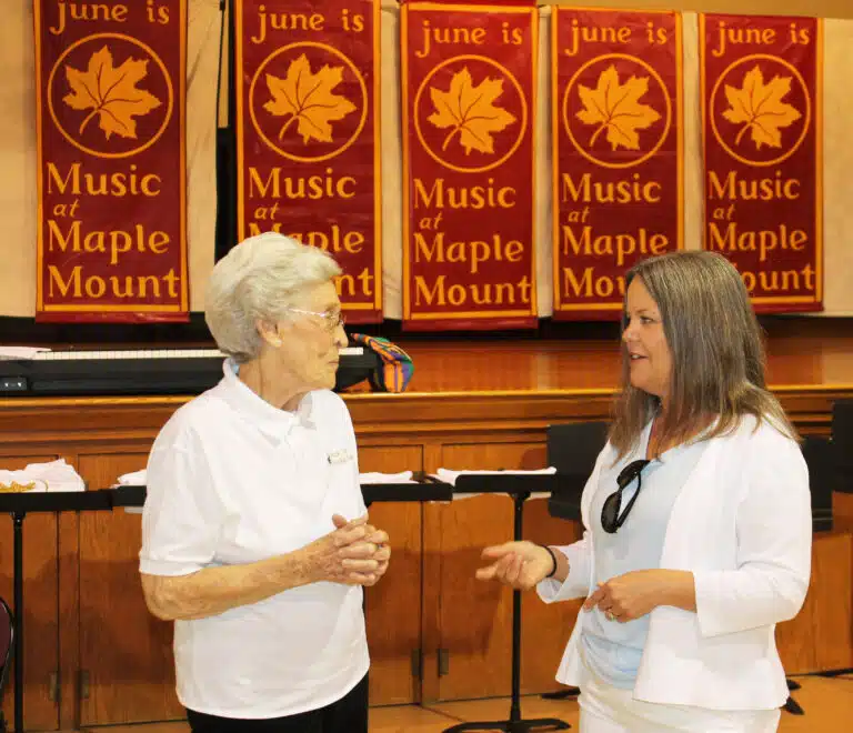 Sister Elaine Burke, left, visits with Tammy Chapman Bisotti in Maple Hall, in front of the display of banners that lined Frederica Street each June when the music camp occurred. Sister Elaine Burke, left, visits with Tammy Chapman Bisotti in Maple Hall, in front of the display of banners that lined Frederica Street each June when the music camp occurred.