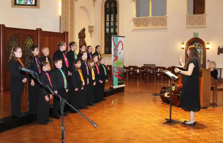 About half of the members of the Kentucky Youth Chorale, led by Madison Wells, sing “The Music Within Us,” written by the late Joy Malone, who was an instructor at the camp. The children also sang two more songs. About half of the members of the Kentucky Youth Chorale, led by Madison Wells, sing “The Music Within Us,” written by the late Joy Malone, who was an instructor at the camp. The children also sang two more songs.