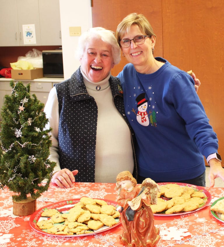Associates Marian Bennett, left, and Risë Karr share a hug over a plate of cookies.