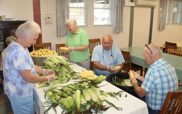 Sister Suzanne Sims, in the light green shirt, is joined by her siblings to shuck and cut corn. At left is her sister, Gertie Frey, and at right are her brothers Steve and Alan Sims. Sister Suzanne Sims, in the light green shirt, is joined by her siblings to shuck and cut corn. At left is her sister, Gertie Frey, and at right are her brothers Steve and Alan Sims.