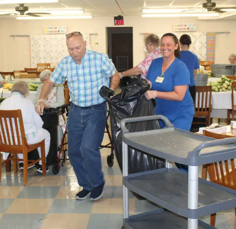 Alan Sims, brother of Sister Suzanne Sims, and Devin Gibson, Food Service cook, haul a bag of corn debris to the trash. Alan Sims, brother of Sister Suzanne Sims, and Devin Gibson, Food Service cook, haul a bag of corn debris to the trash.