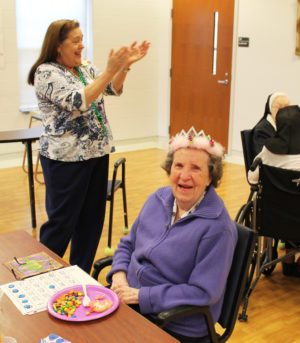 Debbie Dugger, left, activities coordinator for the sisters in Saint Joseph Villa, leads a round of applause after crowning Sister Marie Michael Hayden as the Mardi Gras queen.