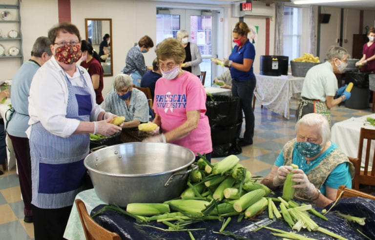 Sister Amelia Stenger, left, and Sister Elaine Burke work to fill another bucket of corn as Sister Catherine Kaufman, right, is on shucking duty.