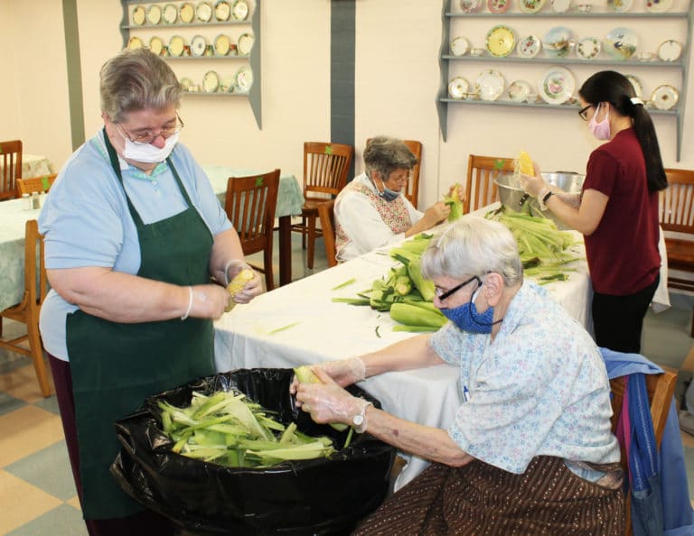 Sister Rose Jean Powers, left, and Sister Shelia Anne Smith, right, fill a can with corn shucks, as Sister Luisa Bickett (background) works with Sister Thoa Phan, a Dominican Sister from Vietnam.