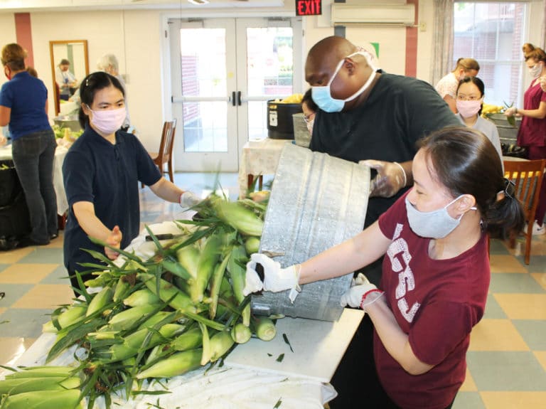 Food Service employee Mario Palmer gets some help from Sister Lang Hoang to dump another bucket of fresh corn on the table, as Sister Hang Nguyen, left, awaits. In the background is Sister Trang Le. The Vietnamese sisters were chopping the ends off the corn to prepare it for shucking.