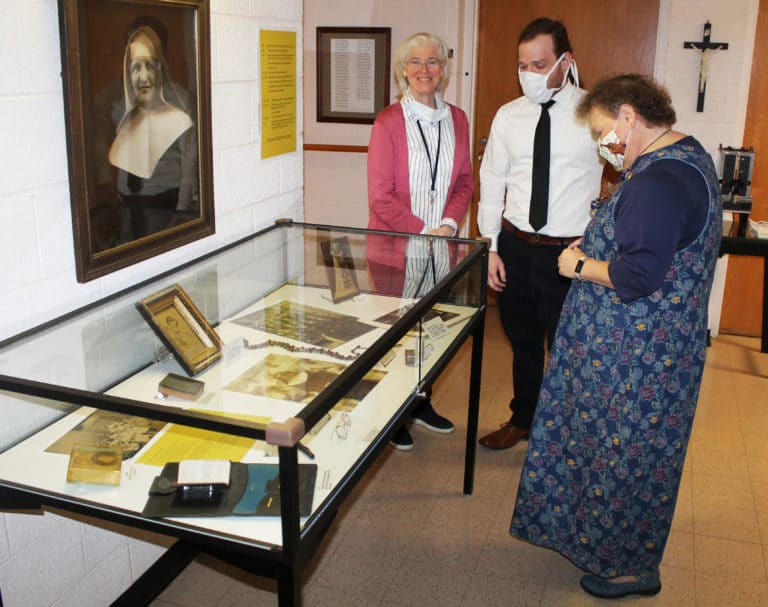 Sister Nancy Liddy, left, Edward Wilson, director of Archives, and Sister Alicia Coomes, director of Local Community Life, look over a display of some of Mother Aloysius’ items that are preserved in the museum. Sister Nancy, who serves in the Archives, led the effort of gathering and researching the items. That’s a photo of Mother Aloysius on the wall.