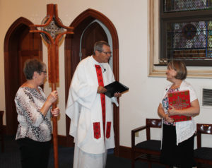 Ursuline Associates Stephanie Render, left, and Joyce York speak with Father Ray Clark prior to Mass. Stephanie carried the cross and Joyce was the first lector.