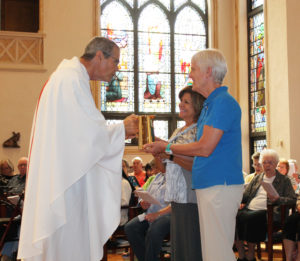 Ursuline Associates Martha House, right, and Debbie Lanham hand the offertory gifts to Father Ray Clark.
