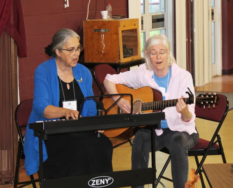Sister Larraine, left, began her comments by joining with Sister Nancy Liddy to lead the singing of “Love is the Boat for the Journey,” by Ian Callanan.