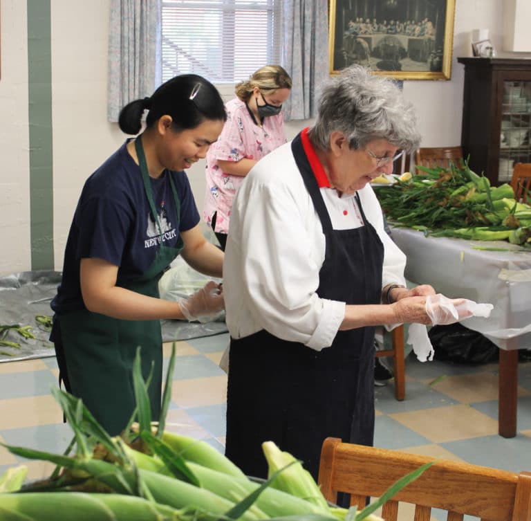 Vietnamese Sister Hang Nguyen, left, helps Ursuline Sister Luisa Bickett with her apron so she could start shucking.